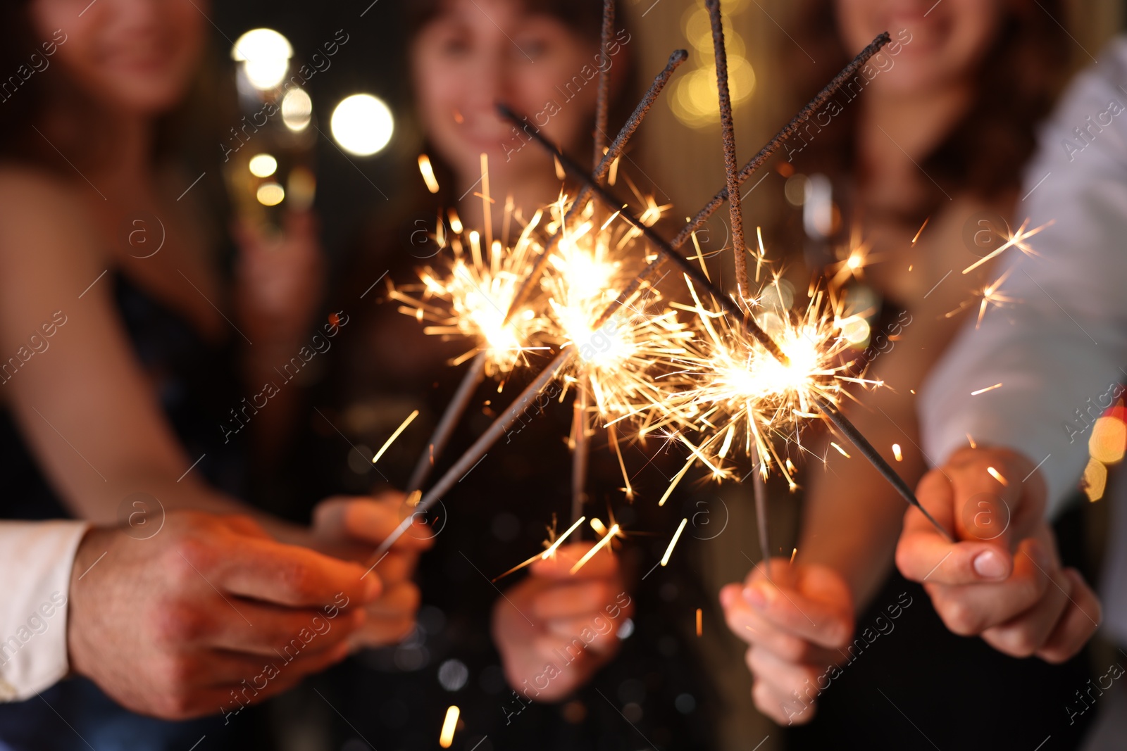 Photo of Friends celebrating New Year with sparklers and wine glasses indoors, closeup
