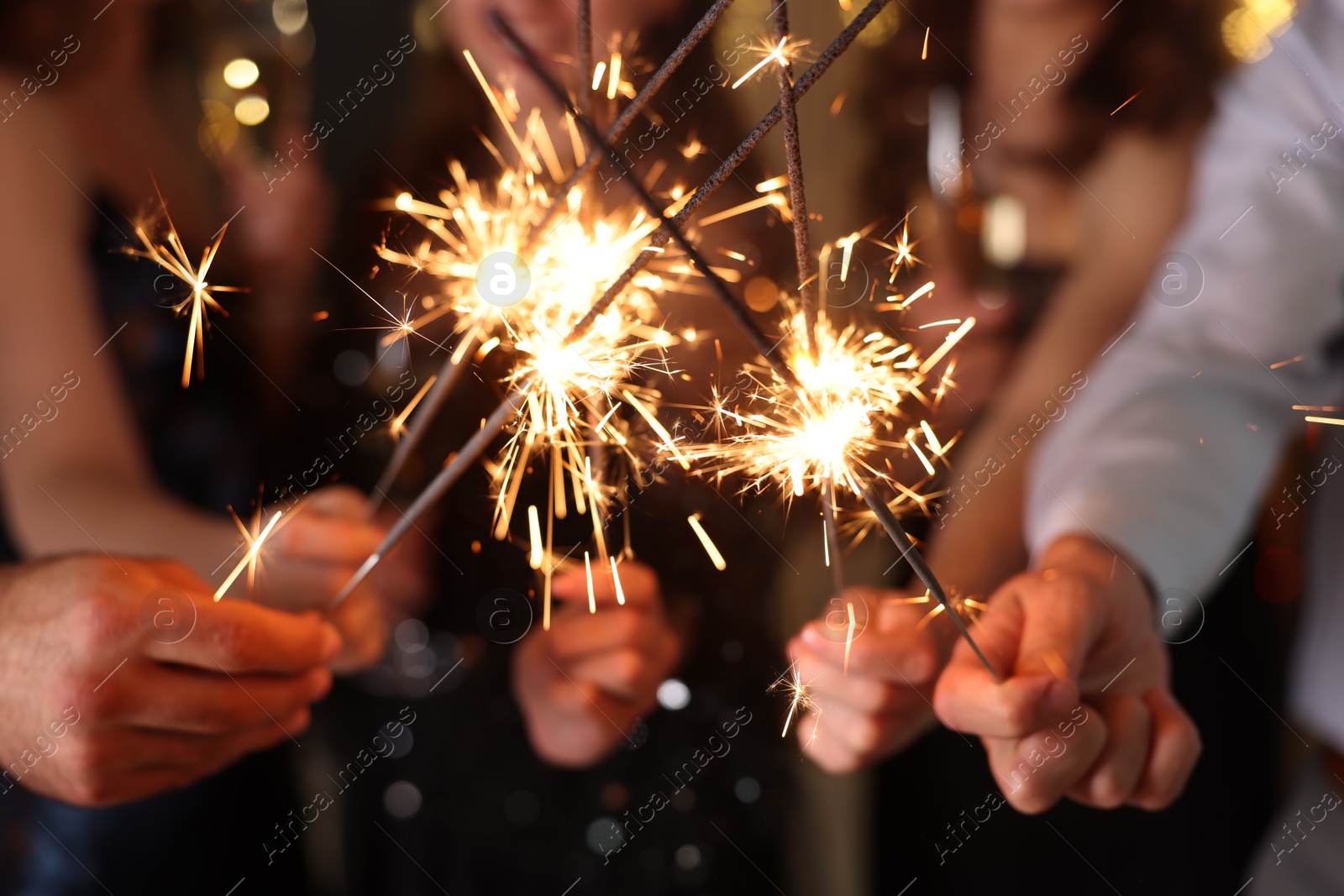 Photo of Friends celebrating New Year with sparklers and wine glasses indoors, closeup