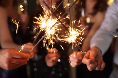 Photo of Friends celebrating New Year with sparklers and wine glasses indoors, closeup