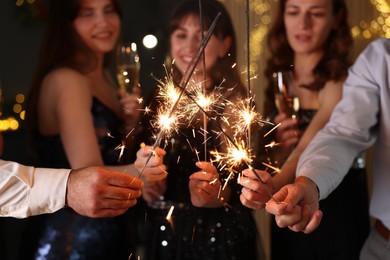 Photo of Friends celebrating New Year with sparklers and wine glasses indoors, selective focus