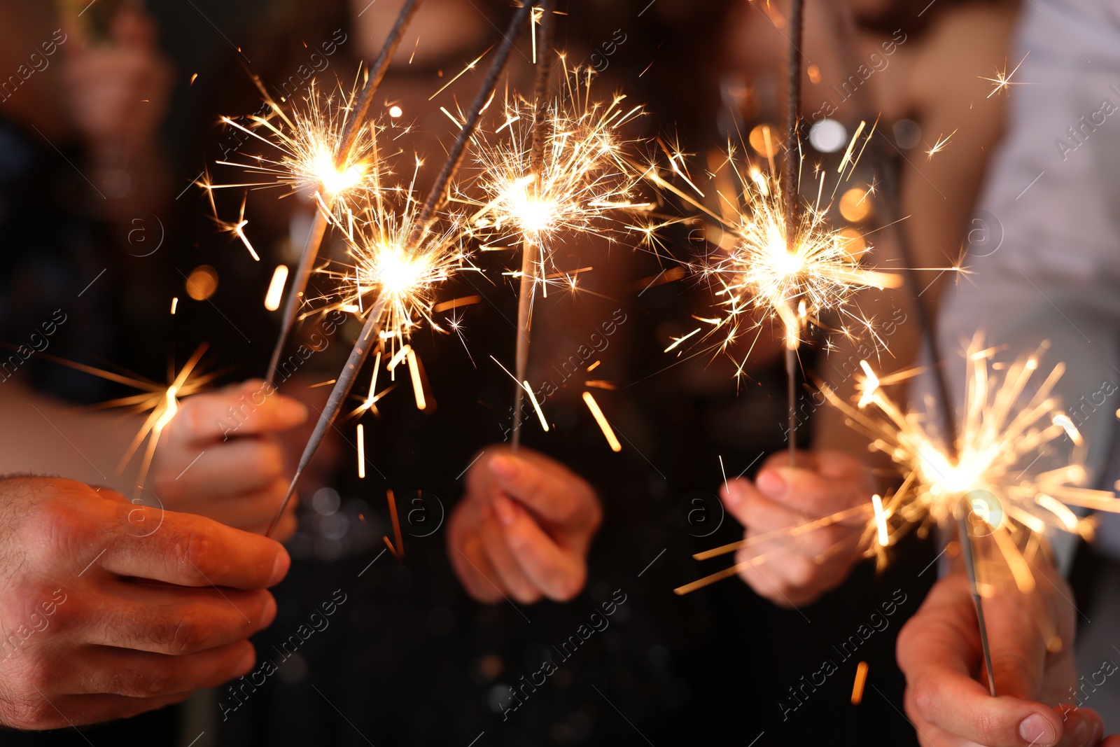 Photo of Friends celebrating New Year with sparklers and wine glasses indoors, closeup