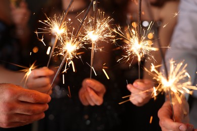 Photo of Friends celebrating New Year with sparklers and wine glasses indoors, closeup