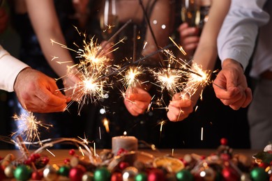 Photo of Friends celebrating New Year with sparklers and wine glasses indoors, closeup