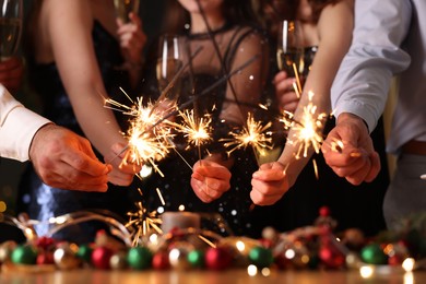 Photo of Friends celebrating New Year with sparklers and wine glasses indoors, closeup