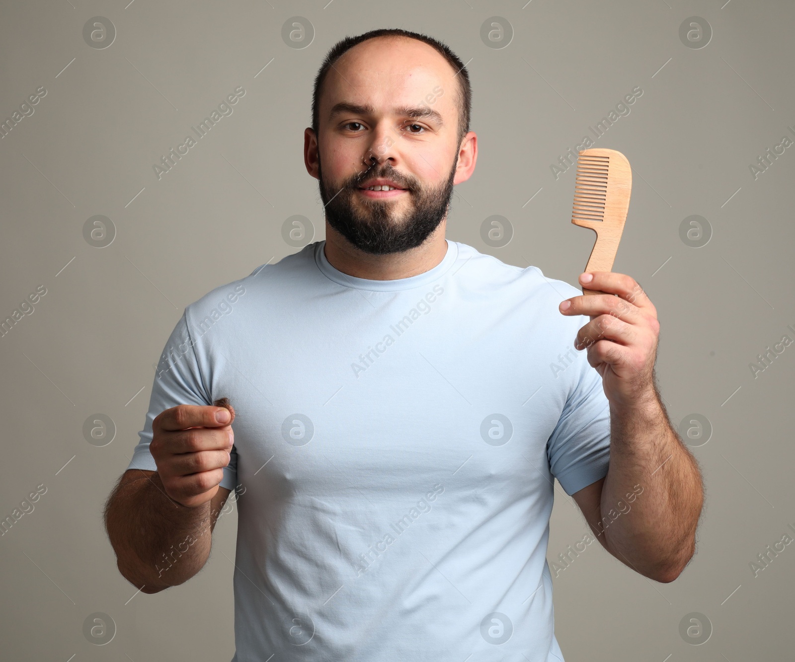 Photo of Baldness problem. Smiling man with comb and clump of lost hair on grey background