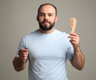 Photo of Baldness problem. Smiling man with comb and clump of lost hair on grey background