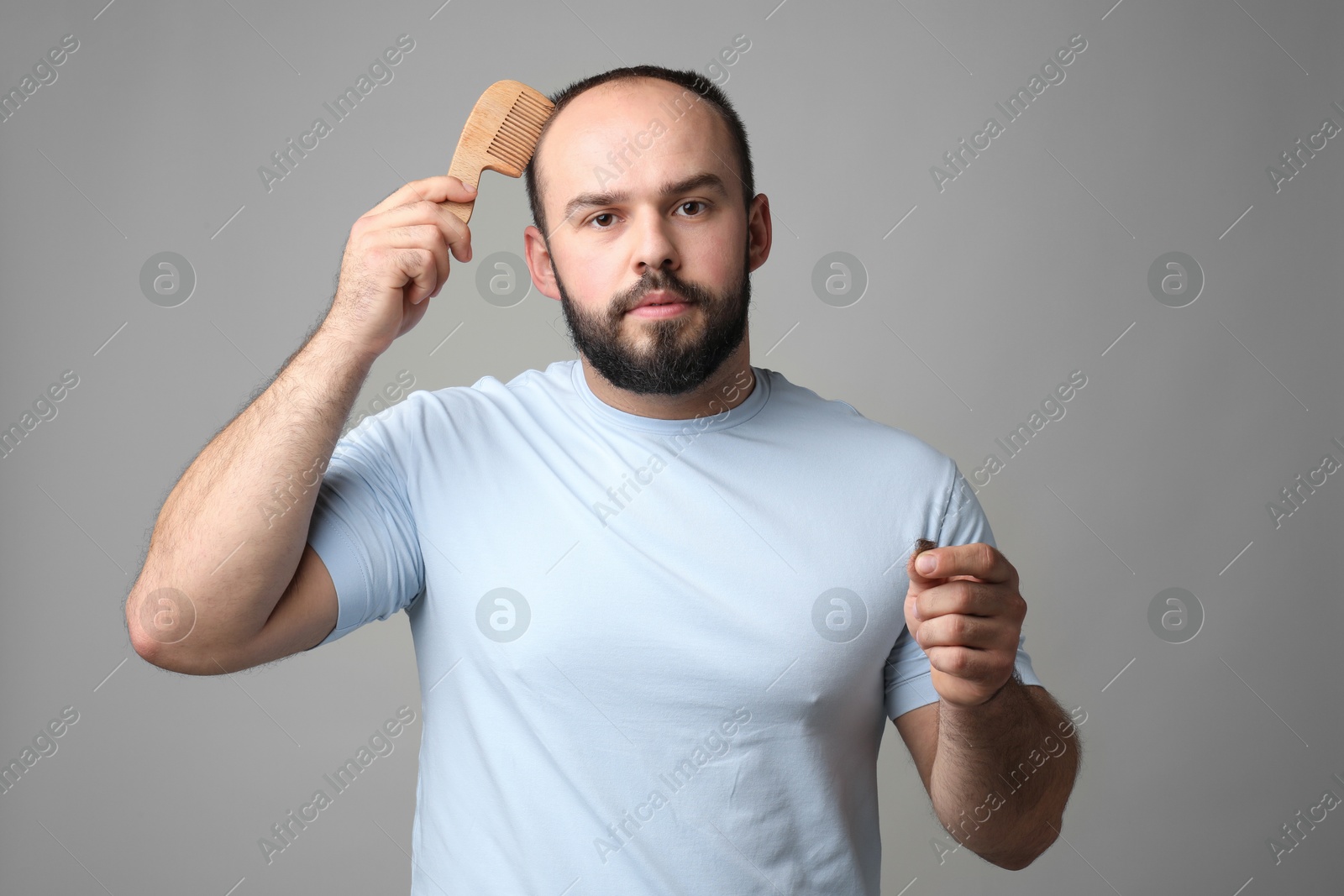 Photo of Baldness problem. Man with comb and clump of lost hair on grey background