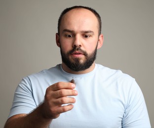 Photo of Baldness problem. Worried man with clump of lost hair on grey background