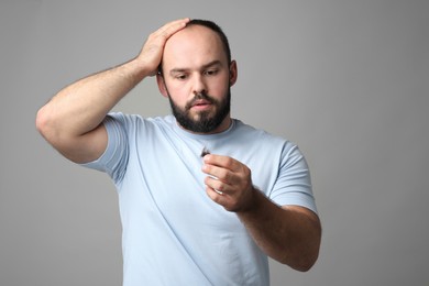 Photo of Baldness problem. Worried man with clump of lost hair on grey background