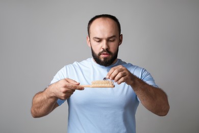 Photo of Baldness problem. Worried man with brush and clump of lost hair on grey background