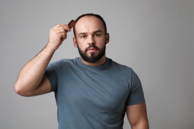 Photo of Baldness problem. Man brushing his hair with comb on grey background