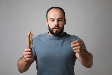 Photo of Baldness problem. Worried man with brush and clump of lost hair on grey background