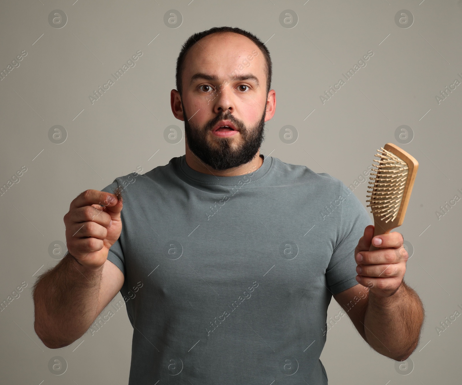 Photo of Baldness problem. Worried man with brush and clump of lost hair on grey background