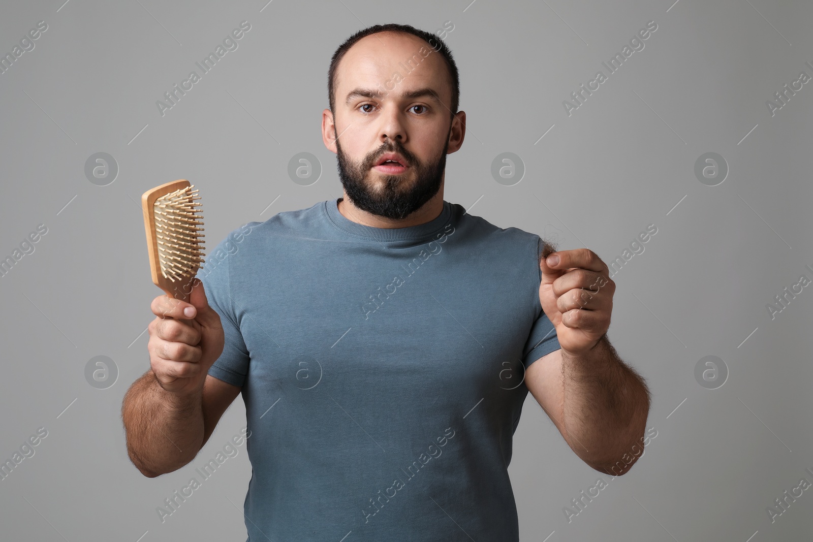 Photo of Baldness problem. Worried man with brush and clump of lost hair on grey background