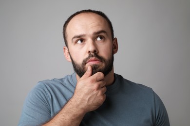 Photo of Baldness problem. Thoughtful man with receding hairline on grey background