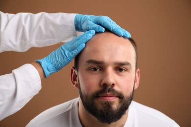 Photo of Baldness problem. Doctor in medical gloves examining patient's head against brown background, closeup