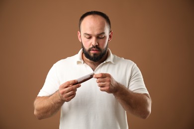 Photo of Baldness problem. Worried man taking his lost hair from comb on brown background