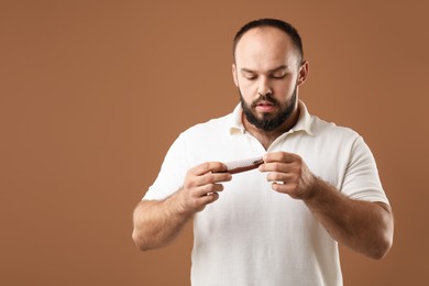 Photo of Baldness problem. Worried man taking his lost hair from comb on brown background. Space for text
