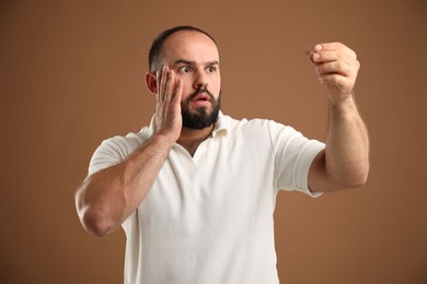 Photo of Baldness problem. Worried man with clump of lost hair on brown background