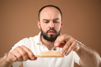 Photo of Baldness problem. Worried man taking his lost hair from brush on brown background