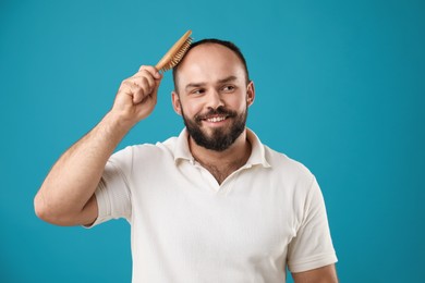 Photo of Baldness problem. Smiling man brushing his hair with comb on light blue background