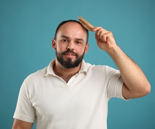 Photo of Baldness problem. Smiling man brushing his hair with comb on light blue background