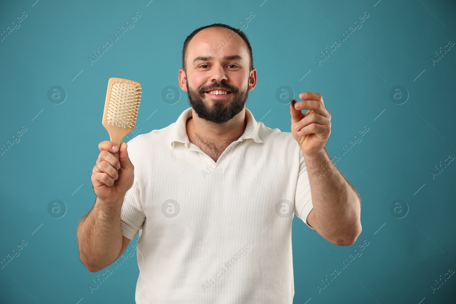 Photo of Baldness problem. Smiling man with brush and clump of lost hair on light blue background