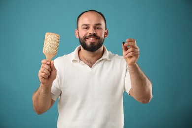 Photo of Baldness problem. Smiling man with brush and clump of lost hair on light blue background