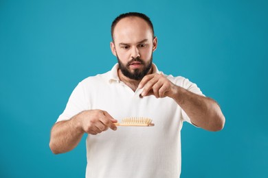 Photo of Baldness problem. Worried man taking his lost hair from brush on light blue background