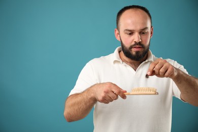 Photo of Baldness problem. Worried man taking his lost hair from brush on light blue background. Space for text