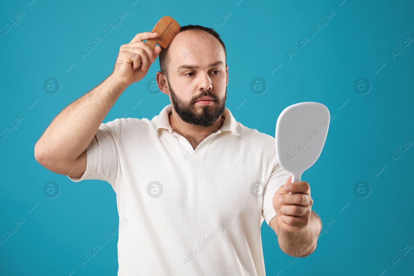 Photo of Baldness problem. Man brushing his hair with comb and looking at mirror on light blue background