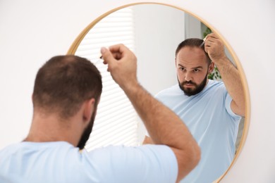 Photo of Baldness treatment. Man applying serum onto his hair near mirror at home