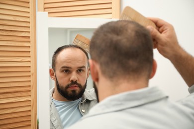 Photo of Baldness problem. Man brushing his hair with comb near mirror at home