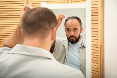 Photo of Baldness treatment. Man applying serum onto his hair near mirror at home