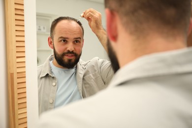 Photo of Baldness treatment. Man applying serum onto his hair near mirror at home