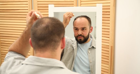 Photo of Baldness treatment. Man applying serum onto his hair near mirror at home
