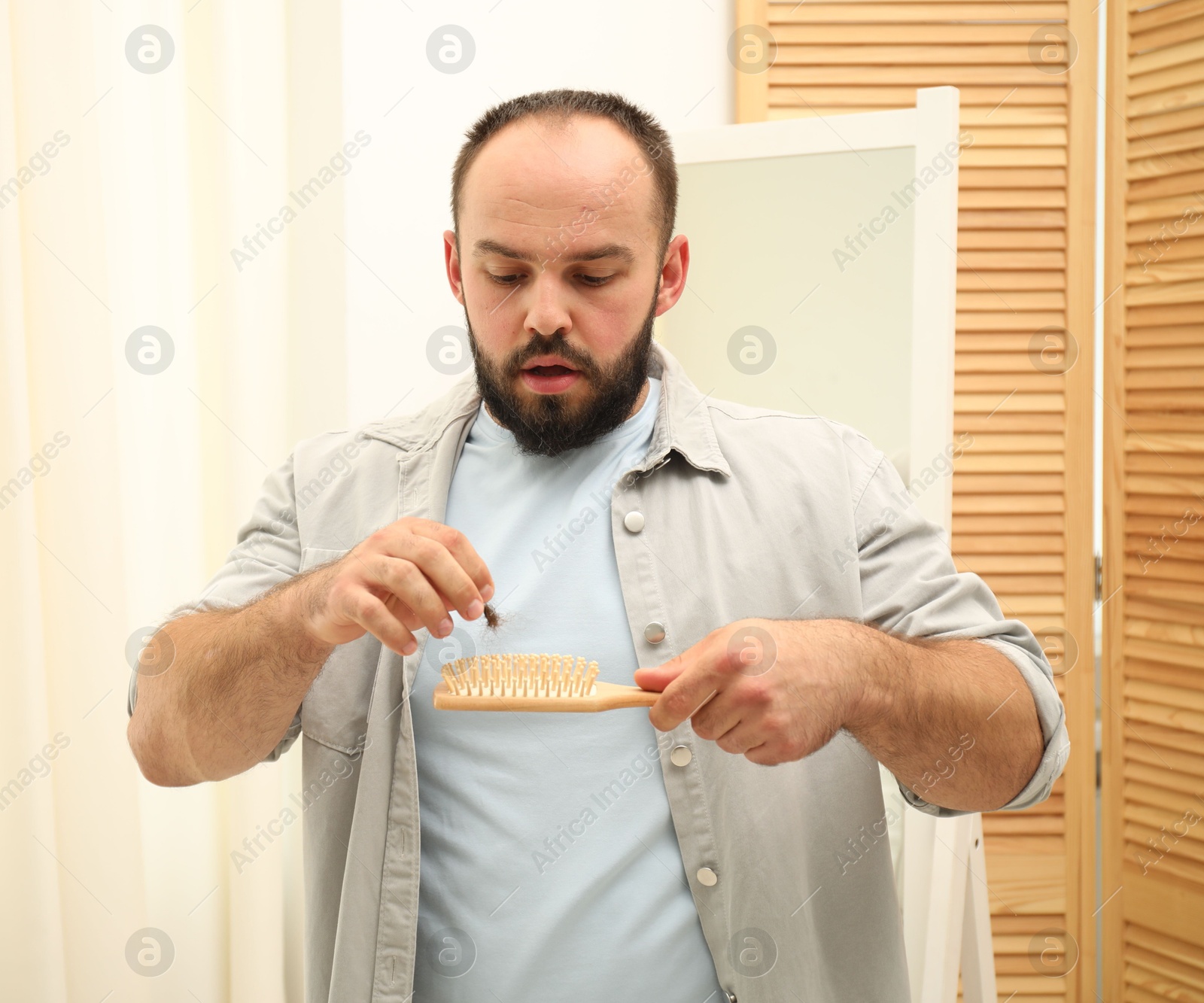 Photo of Baldness problem. Worried man taking his lost hair from brush at home