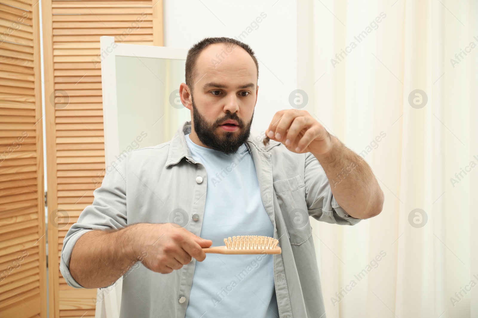 Photo of Baldness problem. Worried man taking his lost hair from brush at home
