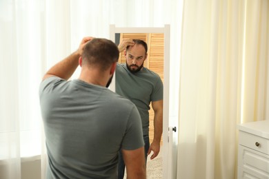 Photo of Baldness problem. Man with receding hairline near mirror at home. Space for text