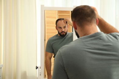 Photo of Baldness problem. Man with receding hairline near mirror at home. Space for text