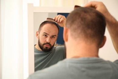 Photo of Baldness problem. Man brushing his hair with comb near mirror at home