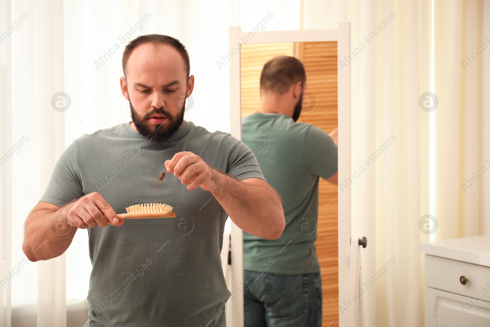 Photo of Baldness problem. Worried man taking his lost hair from brush at home. Space for text