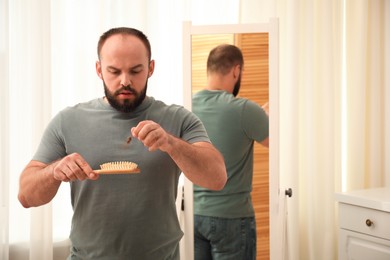 Photo of Baldness problem. Worried man taking his lost hair from brush at home. Space for text