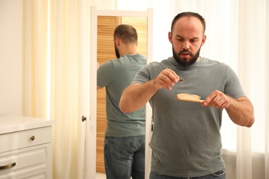 Photo of Baldness problem. Worried man taking his lost hair from brush at home. Space for text