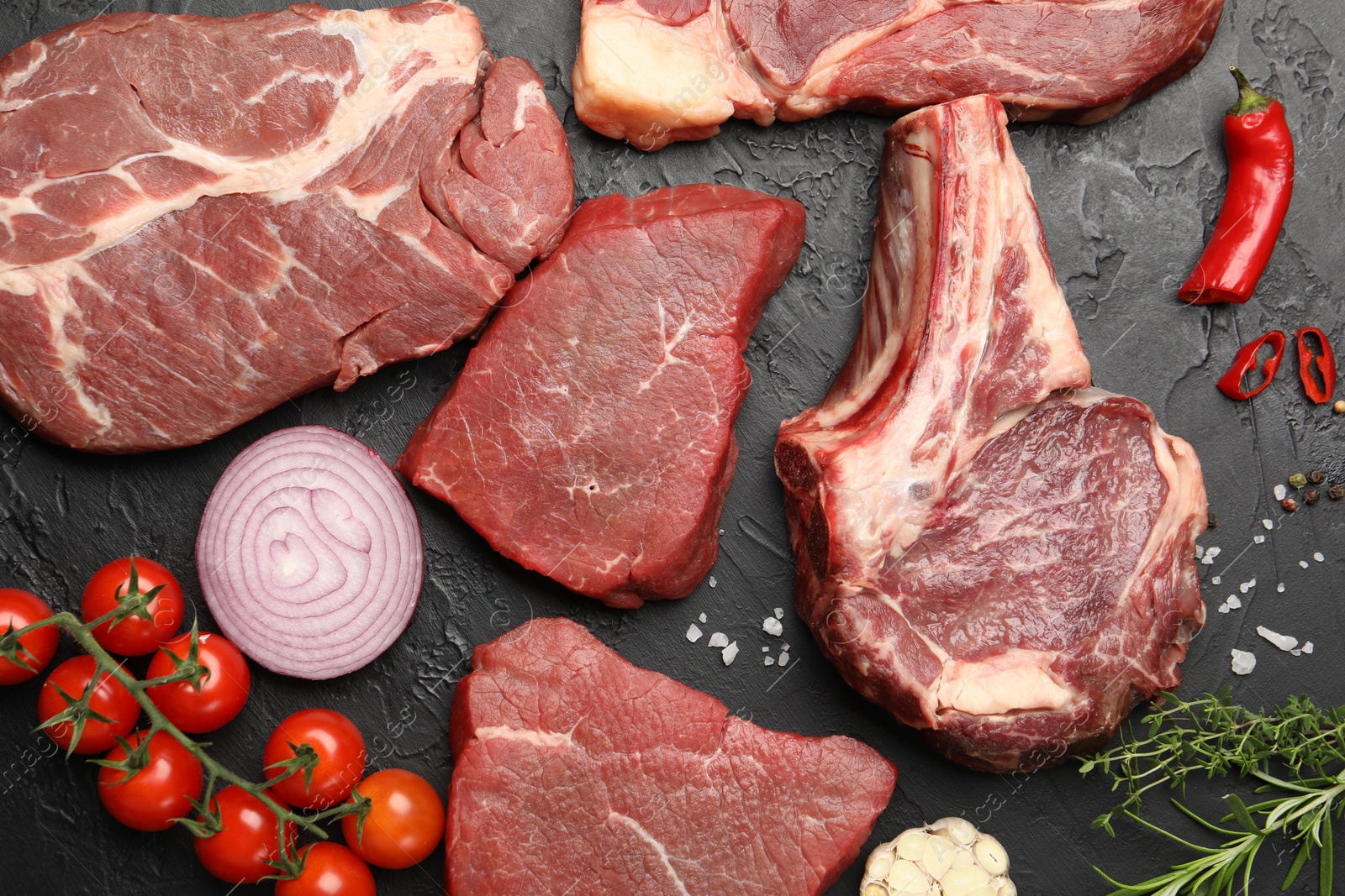 Photo of Pieces of raw beef meat, spices and tomatoes on black table, flat lay
