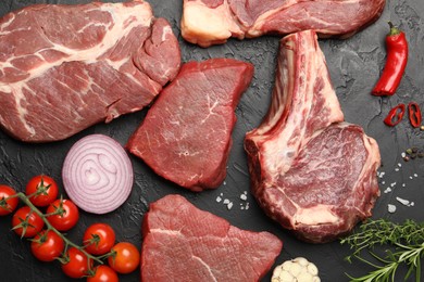 Photo of Pieces of raw beef meat, spices and tomatoes on black table, flat lay