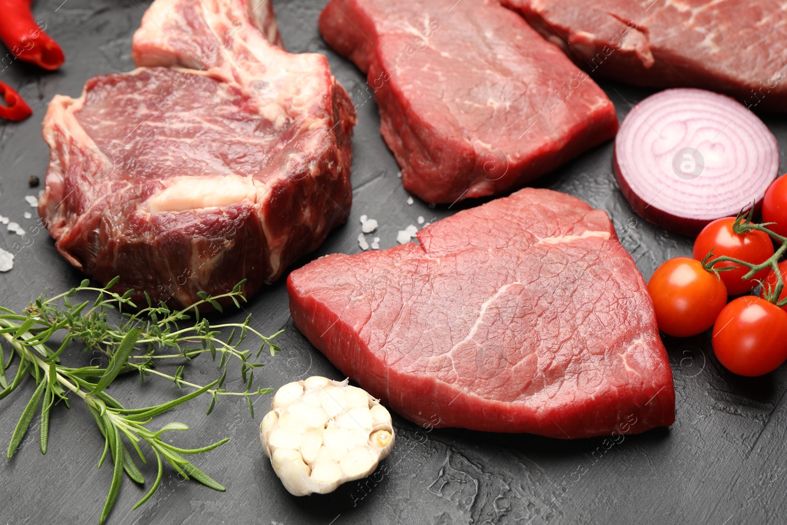 Photo of Pieces of raw beef meat, spices and tomatoes on black table, closeup