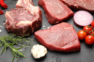 Photo of Pieces of raw beef meat, spices and tomatoes on black table, closeup