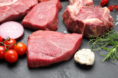 Photo of Pieces of raw beef meat, spices and tomatoes on black table, closeup