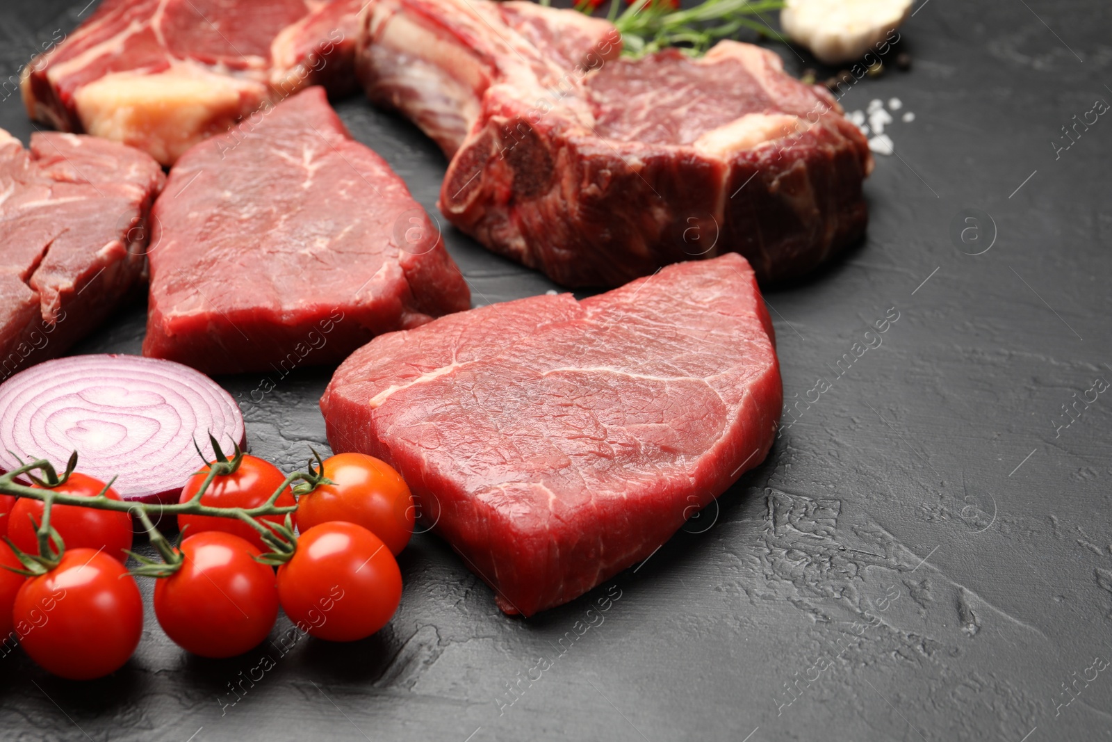 Photo of Pieces of raw beef meat, spices and tomatoes on black table, closeup. Space for text